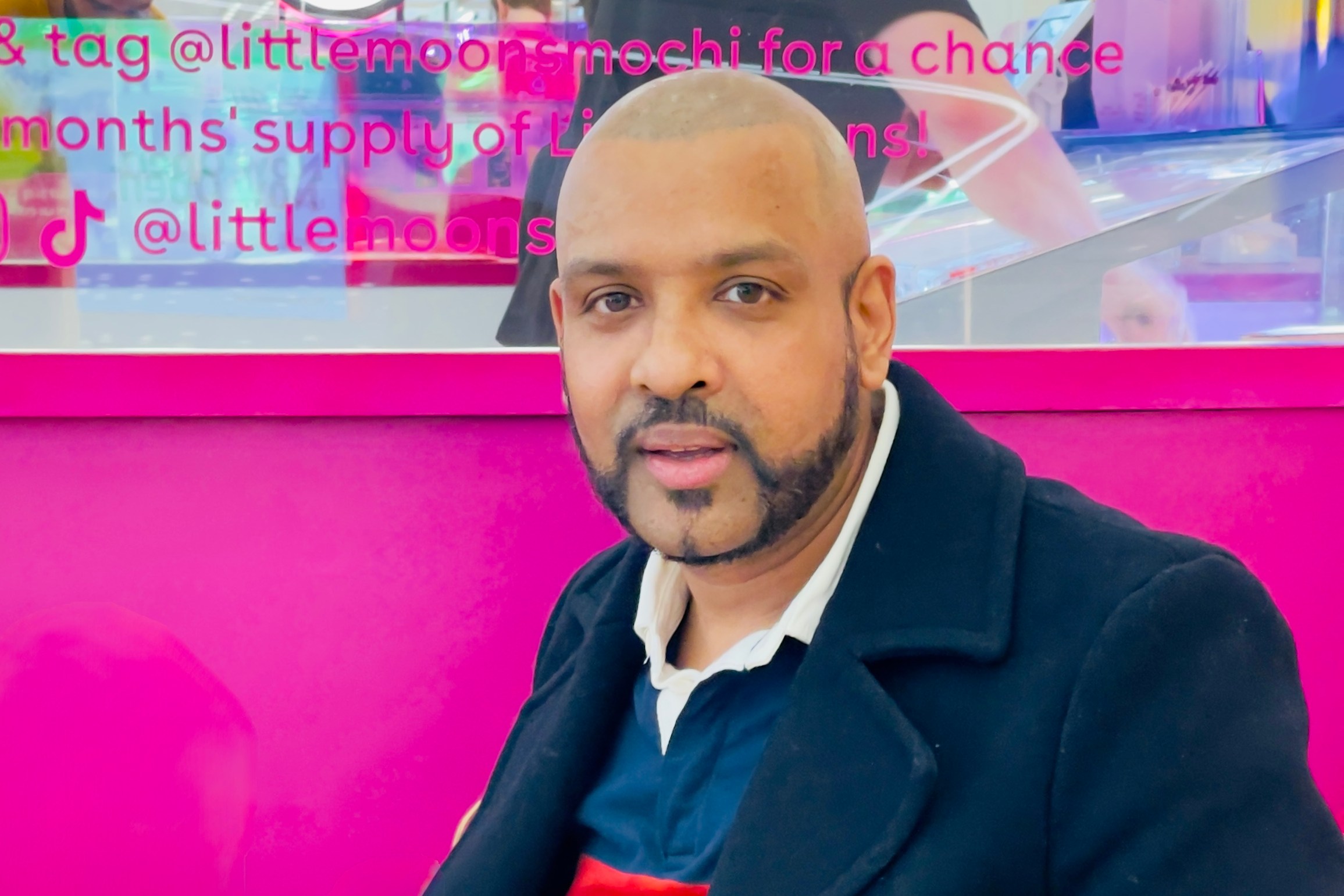 Man sitting on pink bench in front of a mochi ice cream display.