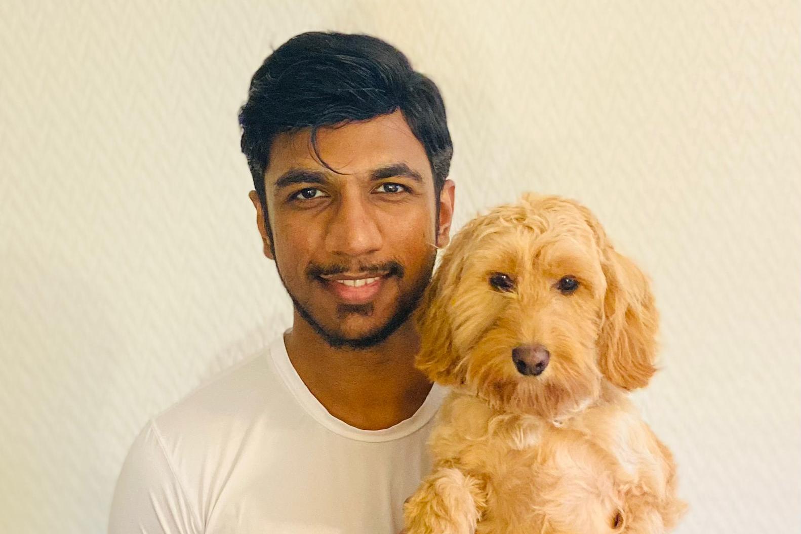 Man holding a small, light brown dog.